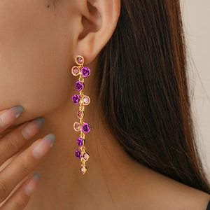 Gros plan de longues boucles d'oreilles dorées avec fleurs mauves et gemmes roses