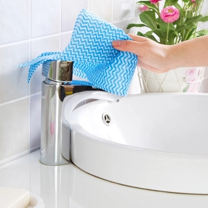 Blue and white wave patterned disposable cleaning cloth wiping a bathroom faucet