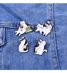 Detail of four cute white cat enamel pins with wine glasses on denim fabric background
