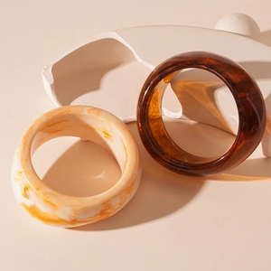Maillard style amber and orange marble resin bracelets on minimalist plaster stands