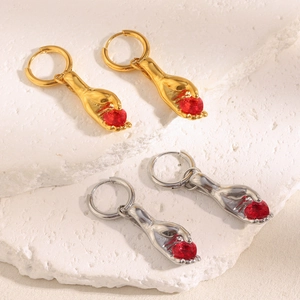 Close-up of gold and silver hand-holding heart earrings on white stone texture