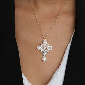 Detail shot of a golden cross necklace with a teardrop zircon worn on a model