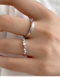 Detail of silver couple rings with star texture and zircon stones on white fabric