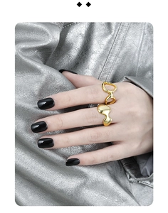 Close-up of two irregular gold molten rings on a hand against metallic fabric