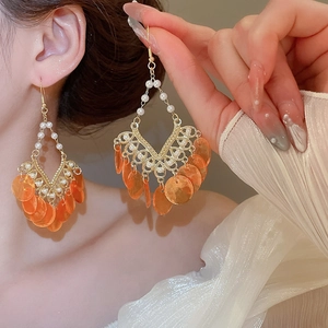 Detailed view of gold shell earrings with orange sequins and pearls worn by a model