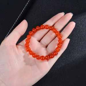 Close-up of vibrant orange-red agate beaded stretch bracelet held in hand against black leather