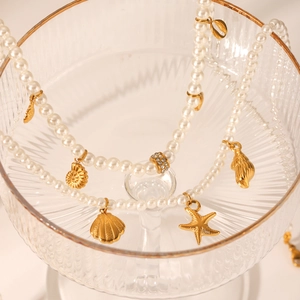 Detailed macro shot of white pearls with golden shell and starfish charms in a glass