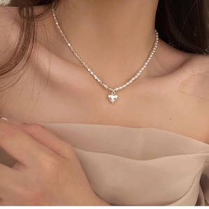 Asymmetric pearl and silver bow heart necklace on woman's neck for elegant look