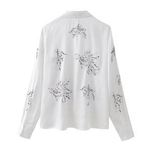 Close-up of white long sleeve shirt with black floral embroidery and beaded detailing