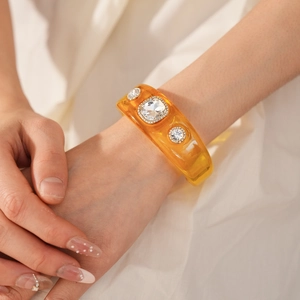 Macro detail of amber resin bangle featuring three sparkling crystals on an elegant model