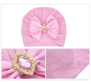 Detailed view of baby turban hat featuring pink satin bow with gemstone embellishment