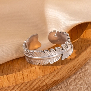 Macro shot of silver feather open ring in stainless steel on a wooden tray with silk