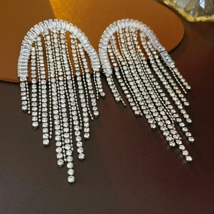 Macro detail of silver tassel earrings with sparkling cubic zirconia on a dark leather surface