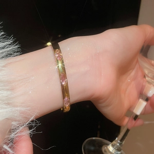 Detailed view of an elegant open gold bangle with three pink marquise stones on a wrist