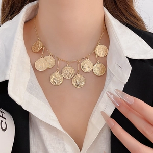 Detailed close-up of a gold multi-coin pendant necklace layered on a white shirt