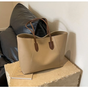 Close-up of khaki tote bag with dark brown handles on a stone display stand