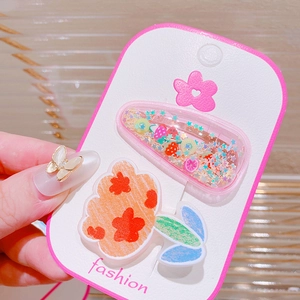 Close-up of glittery pink shaker hair clip and orange flower accessory on card