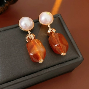 Macro view of vintage earrings with pearl studs and amber resin drops on a jewelry box