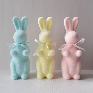 Three flocking Easter rabbit figurines in blue, yellow, and pink with ribbon bows