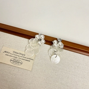 Detailed close-up of long blue shell tassel earrings with white pearls on a wooden frame
