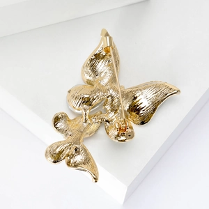 Elegant matte gold butterfly brooch with secure pin back on white geometric base