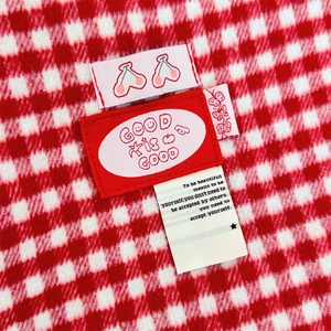 Detailed view of red plaid wool tote bag fabric with decorative cherry and text labels