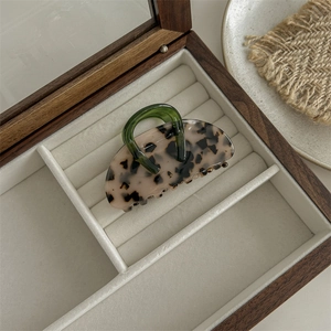 Detailed view of leopard print acetate hair claw clip with a green handle on velvet