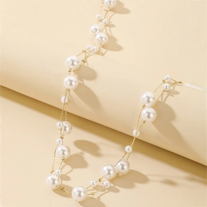 Close-up of layered gold chain necklace featuring multiple white faux pearls on beige stand