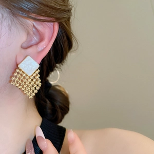Close-up of model wearing geometric woven diamond earrings with gold and white accents