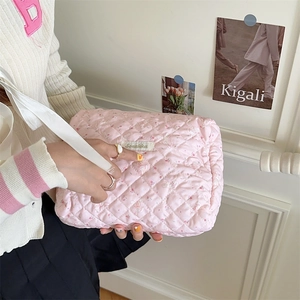 Détail d'une trousse à maquillage matelassée rose avec poignée et étiquette de marque