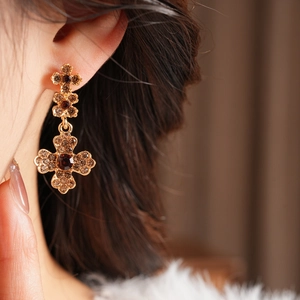 Close-up of vintage golden cross earrings with amber rhinestones on a female model