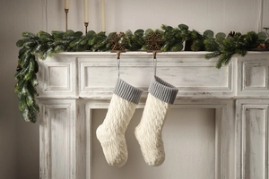 Detail of cable knit Christmas stockings in ivory and grey hanging on a fireplace