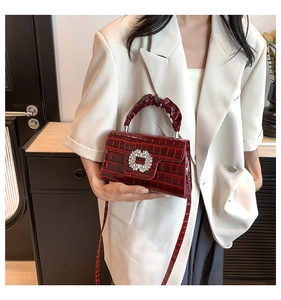 Detail of burgundy crocodile pattern handbag with rhinestone buckle on white blazer