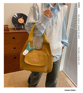 Detail view of yellow canvas tote bag with front pocket and green plush accessory