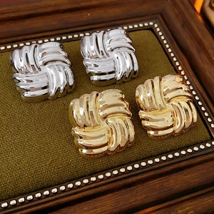 Detailed view of gold and silver square textured knot earrings on a velvet display