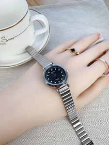 Detail view of small black quartz watch with diamond markers and blue hands on wrist