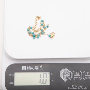 Vue détaillée d'une chaîne en acier doré 18K avec perles de turquoise sur une balance de précision