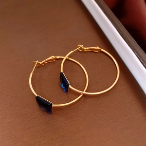 Macro detail of 24k gold-plated hoop earrings featuring deep blue square geometric gemstones