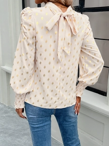 Detail of beige chiffon blouse featuring gold diamond print and a back neck tie bow