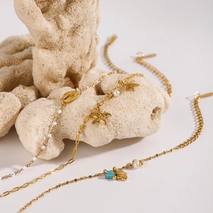 Detailed shot of ocean-style gold chain bracelet with starfish and pearl charms on coral