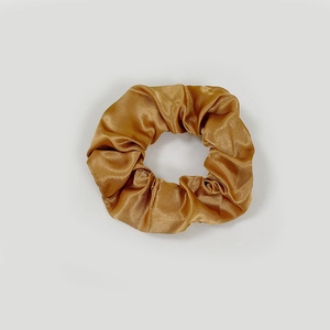 Detailed close-up of glossy champagne satin fabric texture on a pleated scrunchie
