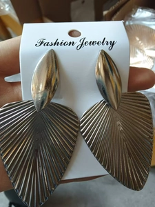 Close-up of large silver leaf earrings with textured radial patterns on white card