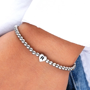 Detail of silver beaded bracelet with heart charm featuring engraved letter R on wrist