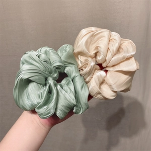 Glossy pleated satin scrunchies in mint green and champagne displayed on a neutral background