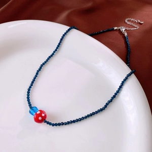 Close-up of beaded necklace with red mushroom pendant and blue beads on white plate