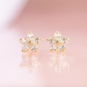 Elegant gold flower stud earrings with zircon petals on a soft pink gradient background