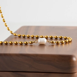 Detail of gold oval bead chain with a natural white freshwater pearl pendant on wood