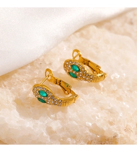 Détail macro de boucles d'oreilles serpent dorées 18 carats avec gemmes vertes et cristaux