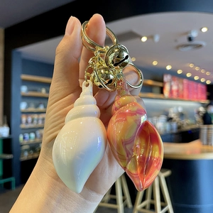 Two colorful iridescent acrylic conch shell keychains with golden bells for bags
