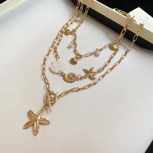 Detail of layered gold necklace featuring starfish, sea shell, and pearl charms
